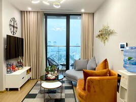 Una sala de estar moderna con un ventanal grande, un televisor de pantalla plana, un dispensador de agua y un área de estar acogedora con un sofá y sillones.