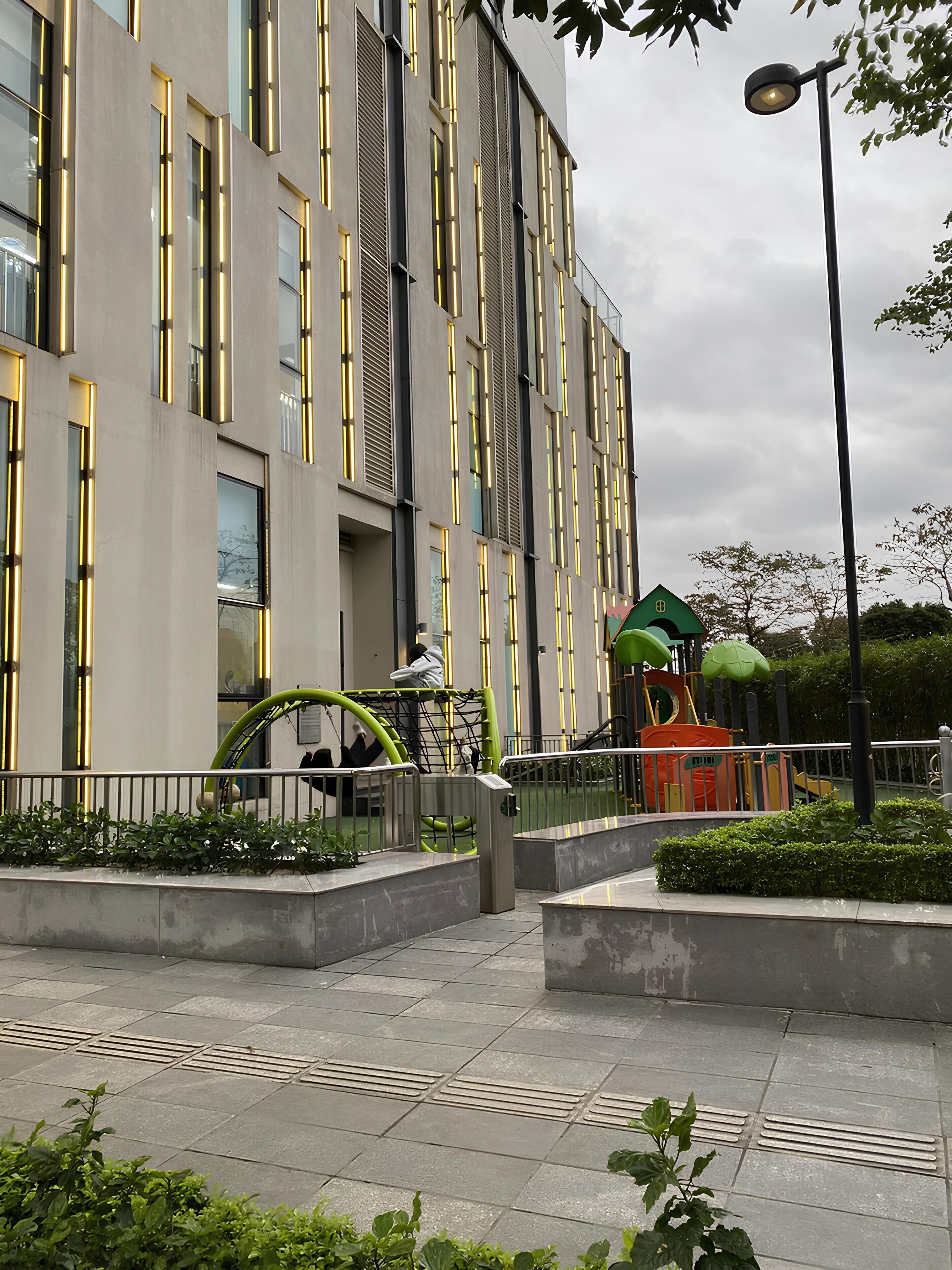 Un edificio moderno con amplios ventanales y un área de juegos con estructuras de colores verde y naranja.