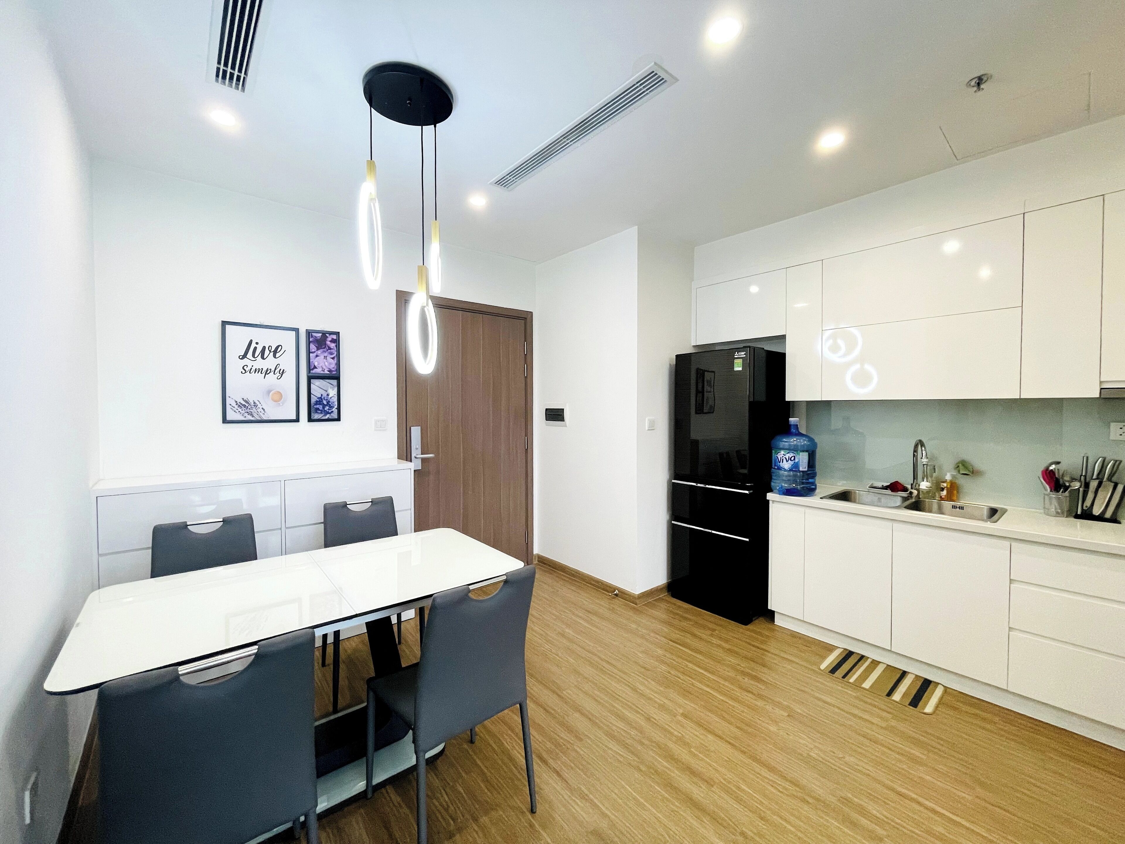 A modern kitchen with white cabinets, a black refrigerator, and a dining area with a white table and chairs.