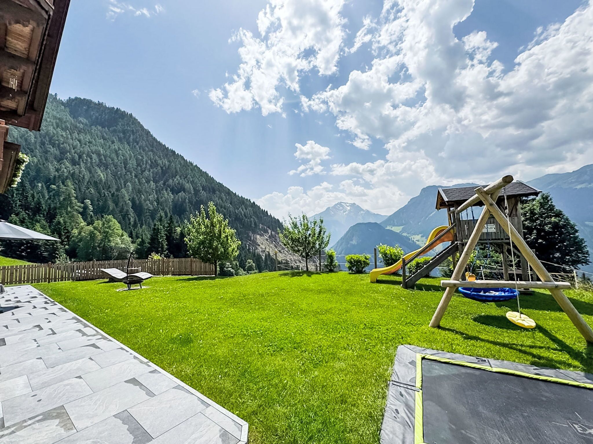 Ein Garten mit Trampolin, einer hölzernen Spielanlage und Blick auf Berge.