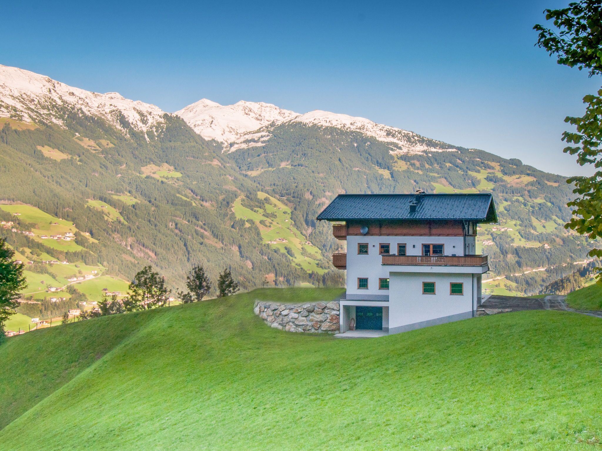 Ein modernes, zweistöckiges Haus mit Steinfundament, einem Balkon und Blick auf eine gebirgige Landschaft.