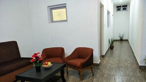 Een woonkamer met een bruine bank, twee rode fauteuils, een zwarte salontafel met fruit en bloemen, en een klok aan de muur.