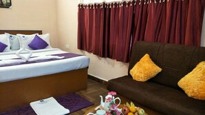 Hotelkamer met een bed, een sofa, een dienblad met ontbijtartikelen en een raam met gordijnen.