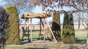 Un portique en bois dans un jardin, avec des haies bien taillées et un ciel dégagé.