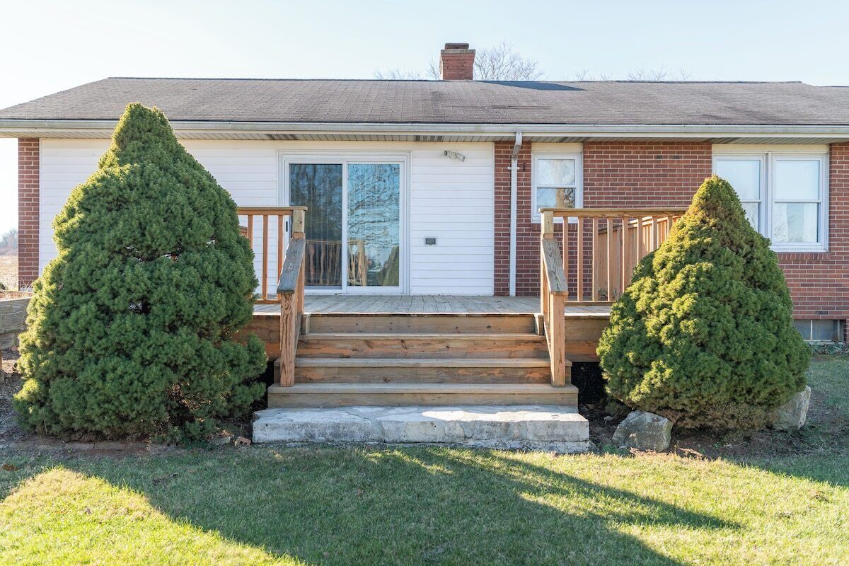 A two-story house with a front porch, a garage, and two well-maintained evergreen trees.