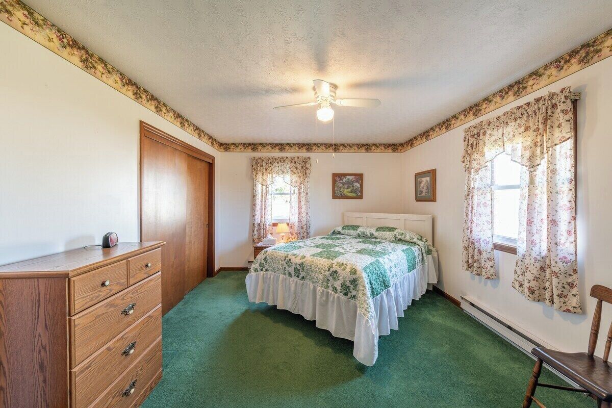 A bedroom with a bed, dresser, ceiling fan, and floral curtains.