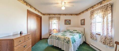 A bedroom with a bed, dresser, ceiling fan, and floral curtains.