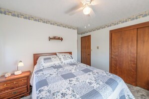 A bedroom with a bed, nightstand, dresser, wooden wardrobe, ceiling fan, and a decorative border on the walls.