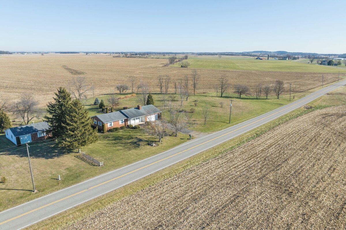 A rural landscape with a road, a house, and open fields.