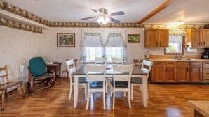 Un coin repas comprenant une table et des chaises, un ventilateur de plafond, des meubles de rangement en bois et une fenêtre avec des rideaux.