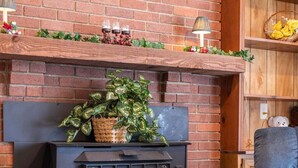 Une cheminée en briques avec un poêle à bois noir, un fauteuil confortable et une étagère ornée de fleurs.
