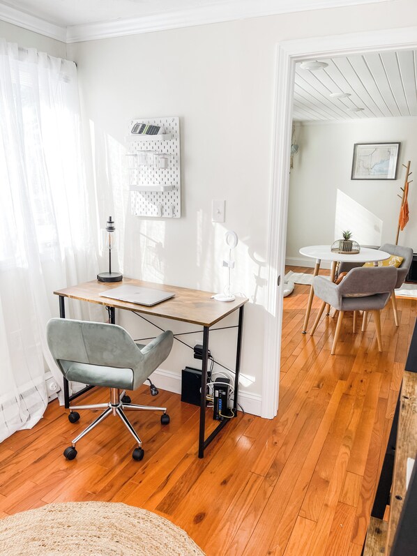 Une pièce moderne et bien éclairée, avec un bureau en bois, une chaise de bureau grise et un coin repas comprenant une table ronde et des chaises.