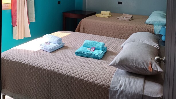 A room with two beds, a ceiling fan, and a TV mounted on the wall. - Casa chikuwa  (San Juan La Laguna)