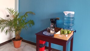 A room with a blue wall, a flat-screen TV mounted above a wooden table, a potted plant, and a water dispenser. - Casa chikuwa  (San Juan La Laguna)