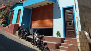 A modern two-story building with a glass balcony, a closed garage door, and a motorcycle parked in front. - Casa chikuwa  (San Juan La Laguna)