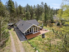 Une maison moderne dotée d’une grande terrasse, entourée d’une forêt.