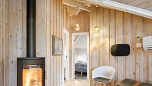 Una habitación acogedora con paneles de madera, una estufa de leña, una silla blanca y un aparador.