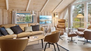Interior acogedor de una cabaña con techo de madera, un ventanal con vista a un lago, un sofá, sillas y una mesa.
