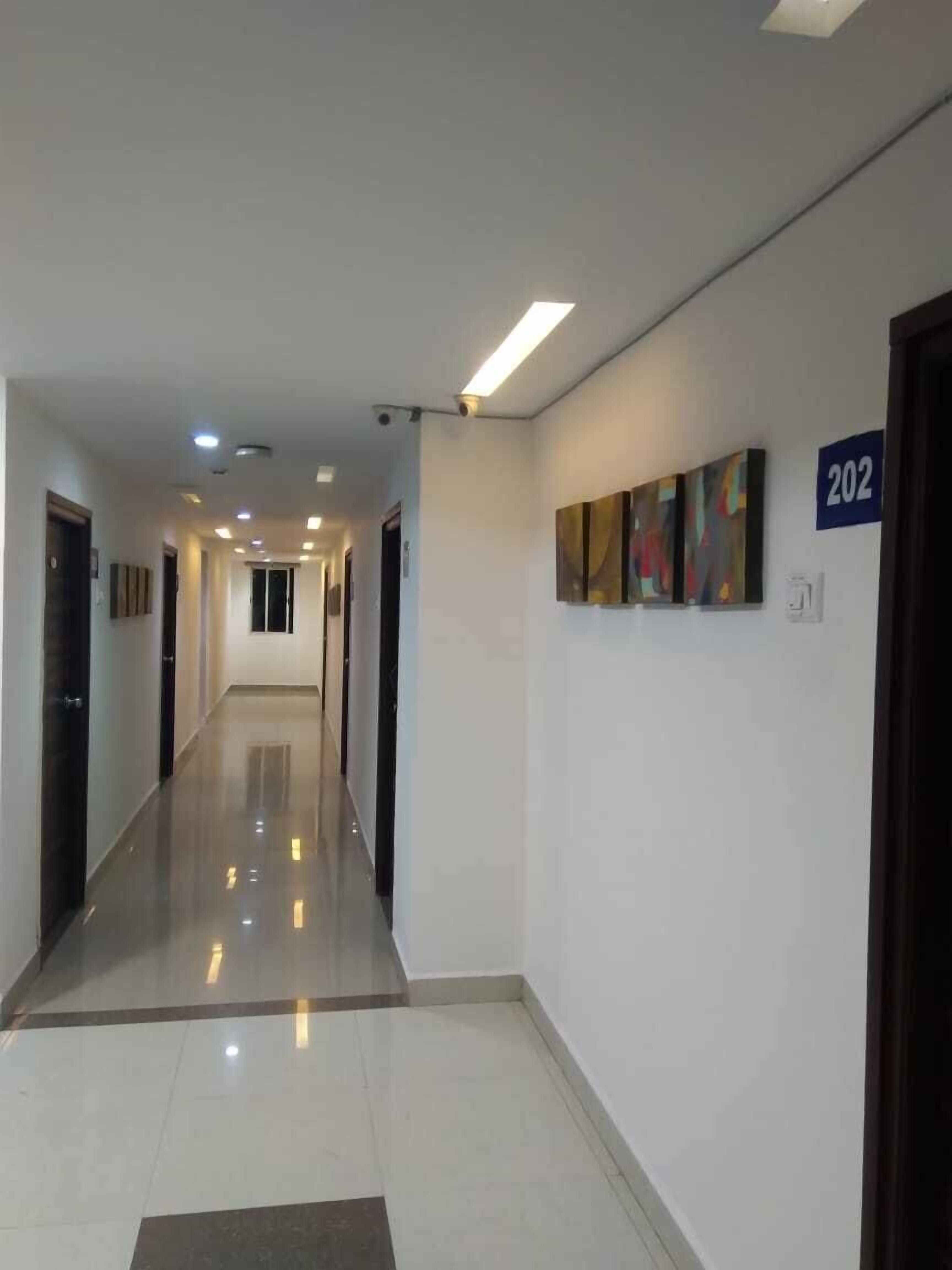 A clean, well-lit hallway with a reflective floor, numbered doors, and abstract art on the walls.