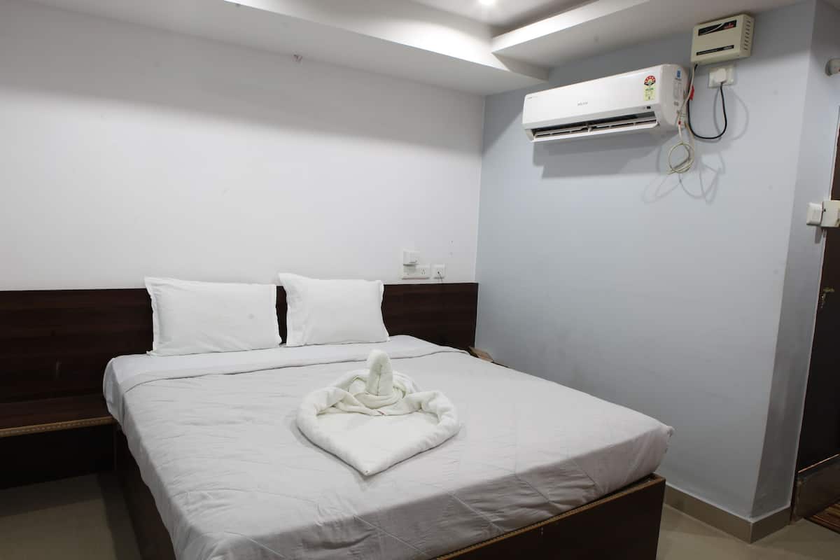 Ein Hotelzimmer mit Bett, weißen Leinen, einem Holz-Kopfteil, einer Klimaanlage und einer Steckdose.