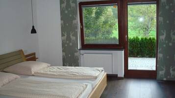 Ein Schlafzimmer mit zwei Betten, einem Fenster mit Blick auf Grünflächen, einem Heizkörper und einer Pendelleuchte.