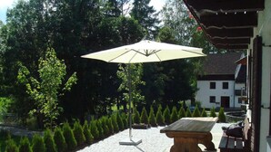 A courtyard with a stone table, a wooden bench, and a large umbrella. - Apartment 'Ferienwohnungen Memminger' with Private Terrace and Wi-Fi (Aicha vorm Wald)