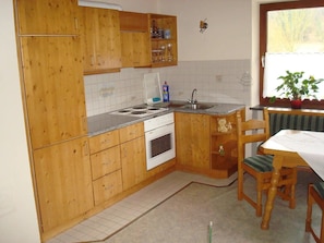A kitchen with wooden cabinets, a stove, a sink, and a dining area with a table and chairs. - Apartment 'Ferienwohnungen Memminger' with Private Terrace and Wi-Fi (Aicha vorm Wald)