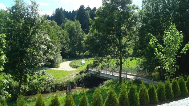 A paved pathway, a bridge, and a green landscape with trees and a small water body. - Apartment 'Ferienwohnungen Memminger' with Private Terrace and Wi-Fi (Aicha vorm Wald)