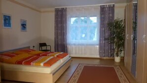 Un dormitorio con cama, una silla, un ventanal con cortinas y una planta en maceta.