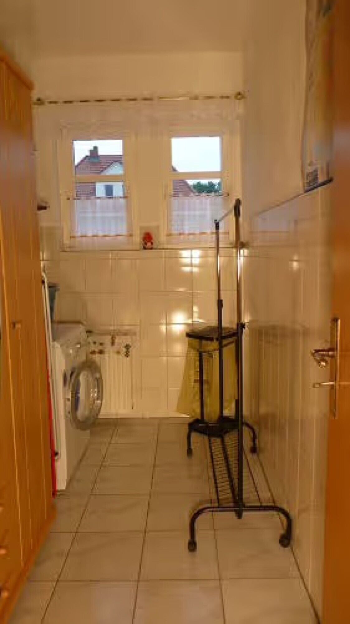 A kitchen with white tiles, a window, a washing machine, and a metal cart.