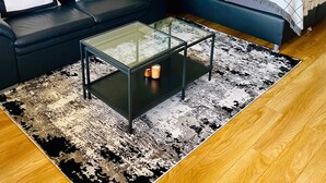 Un salon moderne avec un canapé, un lit, une table basse en verre et un tapis à motifs.