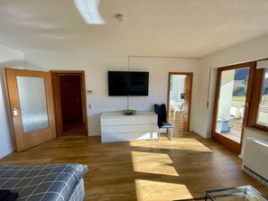 Une pièce avec un plancher en bois, un lit, une commode blanche, un téléviseur et une chaise.
