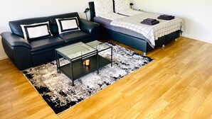 Un salon moderne avec un canapé en cuir noir, une table basse en verre, un canapé-lit bleu et un tapis à motifs.