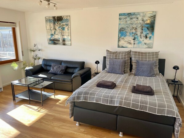 Une chambre à coucher moderne avec un lit, un canapé, une table basse en verre et deux tableaux accrochés aux murs.