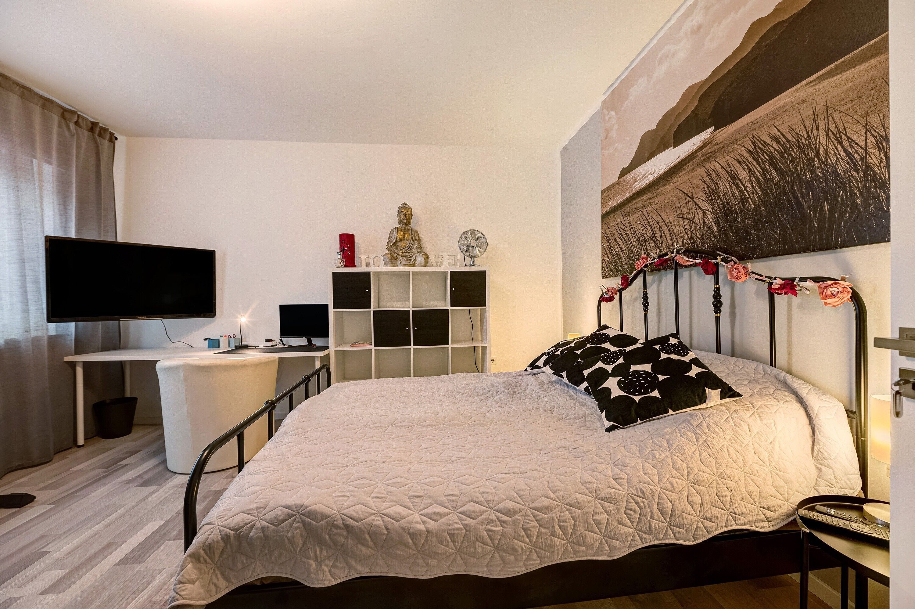 Ein Hotelzimmer mit einem Bett, einem Schreibtisch, einem Fernseher, einem Regal mit Dekoration und einer Wand mit strukturierter Gestaltung.