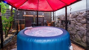 Un bain à remous sous une tonnelle rouge, entouré de murs de pierre et d’une clôture en bois.