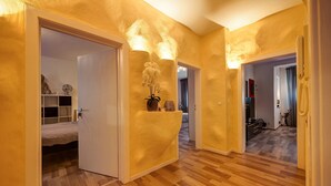 Un couloir avec un plancher en bois, un lit dans la pièce de gauche, un vase de fleurs et un téléphone dans la pièce de droite.