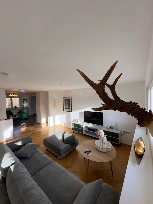 Un salon moderne avec un grand canapé, une table basse ronde, un téléviseur et un élément de décoration original en forme de bois de cerf.