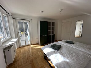Une chambre à coucher comprenant un lit, une armoire, un radiateur et une porte-fenêtre coulissante donnant sur un espace extérieur.