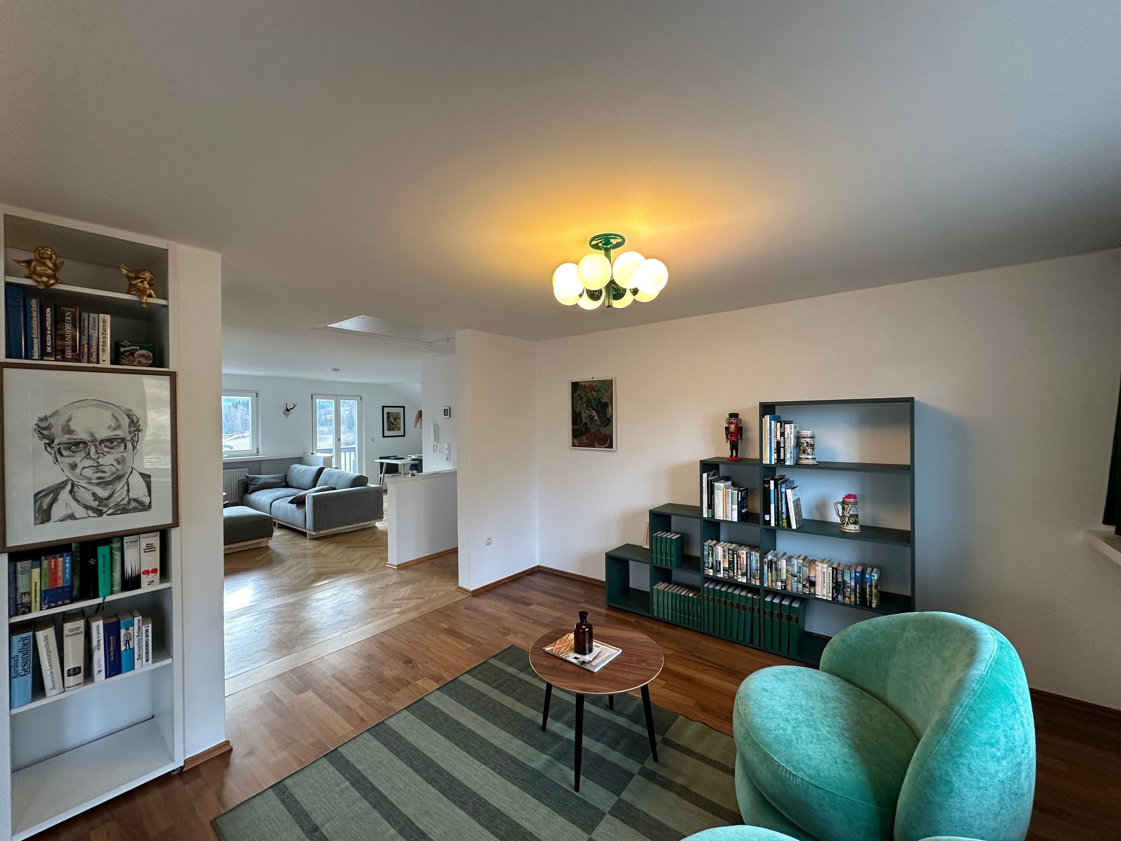 Un salon moderne avec un canapé, un fauteuil turquoise, une table basse et une bibliothèque.