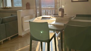 A modern living room with a dining area, large windows, a radiator, and a view of the outside.