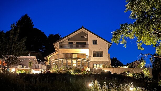A two-story house with a balcony, surrounded by trees and a grassy area.