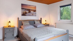 A bedroom with a bed, two bedside tables with lamps, a window with a view, and a painting on the wall.