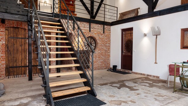 A staircase with wooden steps and metal railings, a brick wall, and a door with a wooden frame.