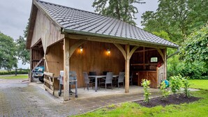 A rustic wooden building with a covered patio, outdoor seating, and a vehicle parked outside.