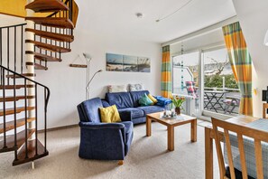 A living room with a blue sofa, a wooden coffee table, a spiral staircase, and a large window with curtains.