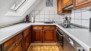 A kitchen with wooden cabinets, a white countertop, a built-in oven, and a window above the sink. - Apartment 'Utspann' with Balcony and Wi-Fi (Sankt Peter-Ording)