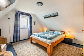 Ein Schlafzimmer mit einem hölzernen Bett, einem Nachttisch, einer Lampe, einem Fenster mit Vorhängen und einem Gemälde an der Wand.