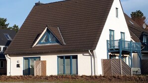Une maison à deux étages avec un toit en pente, un balcon au deuxième étage et un petit porche.