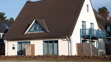 Ein zweistöckiges Haus mit geneigtem Dach, einem Balkon im zweiten Stock und einer kleinen Veranda.